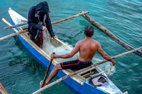 Two fishermen paddling a wooden outrigger boat across clear turquoise water